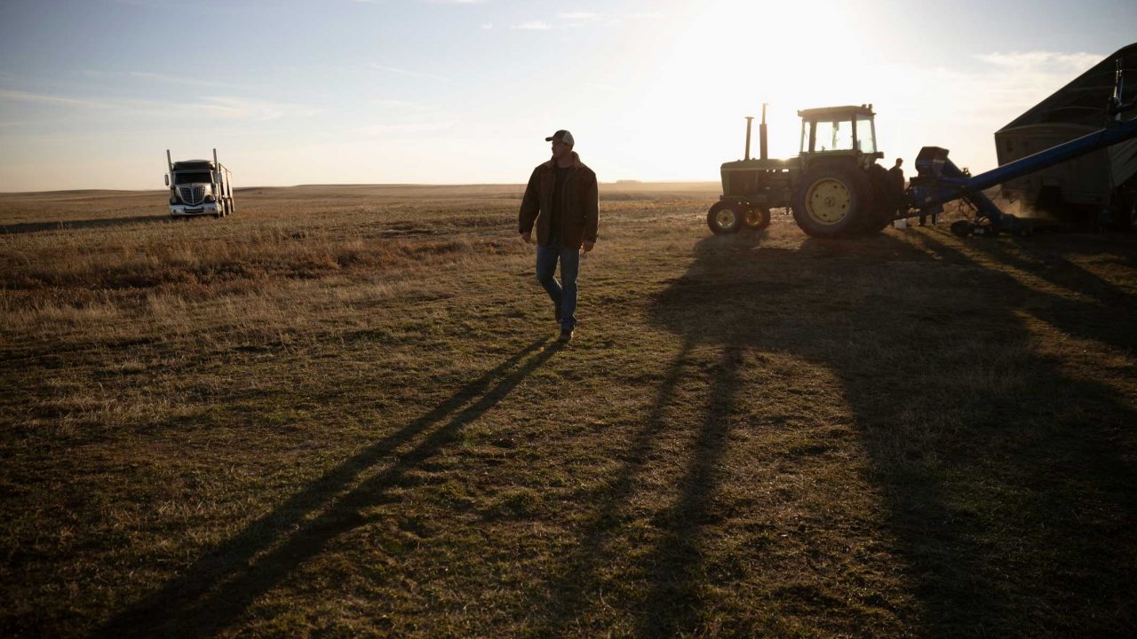 man walking in the country with a tractor and truck behind him