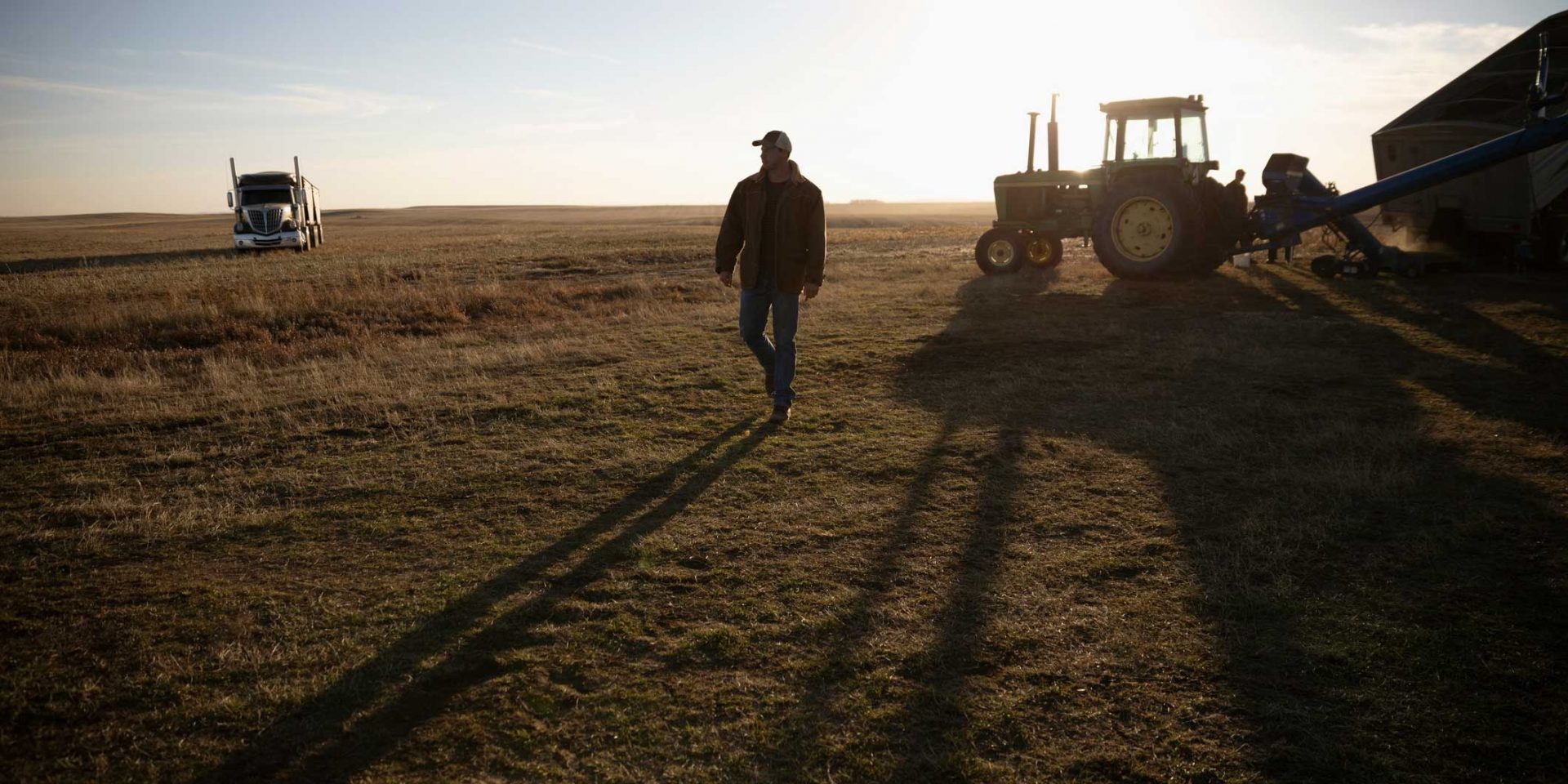 man walking in the country with a tractor and truck behind him
