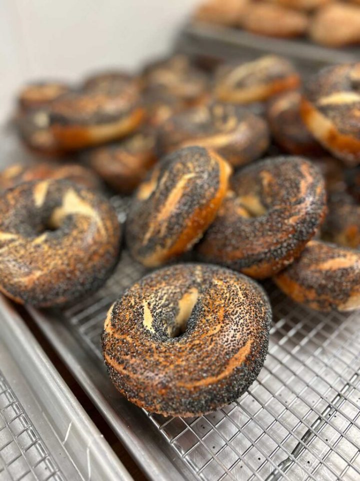 Freshly baked poppy seed bagels cooling on trays, highlighting food manufacturing and bakery production.