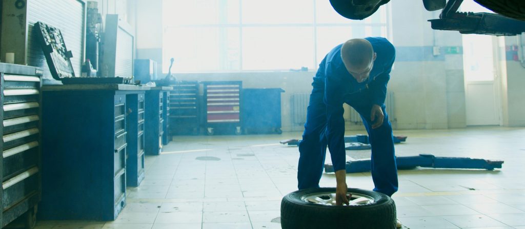 Mechanic in car shop picking up tire from the ground.