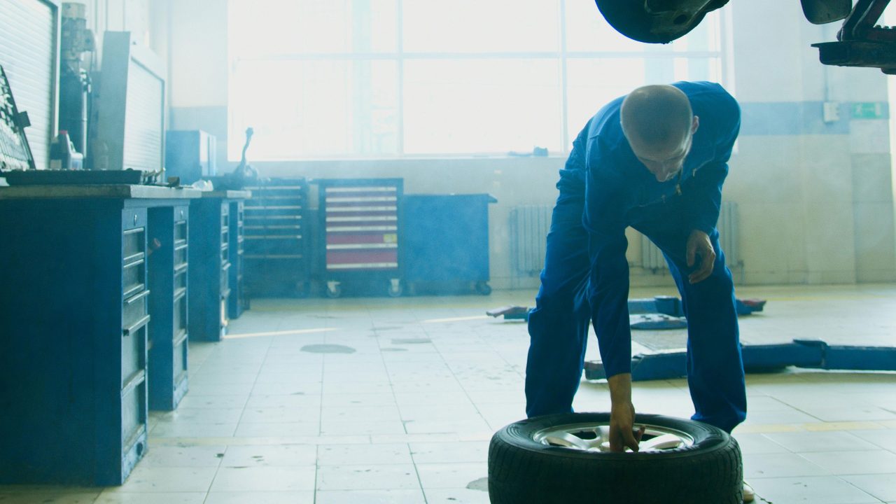Mechanic in car shop picking up tire from the ground.