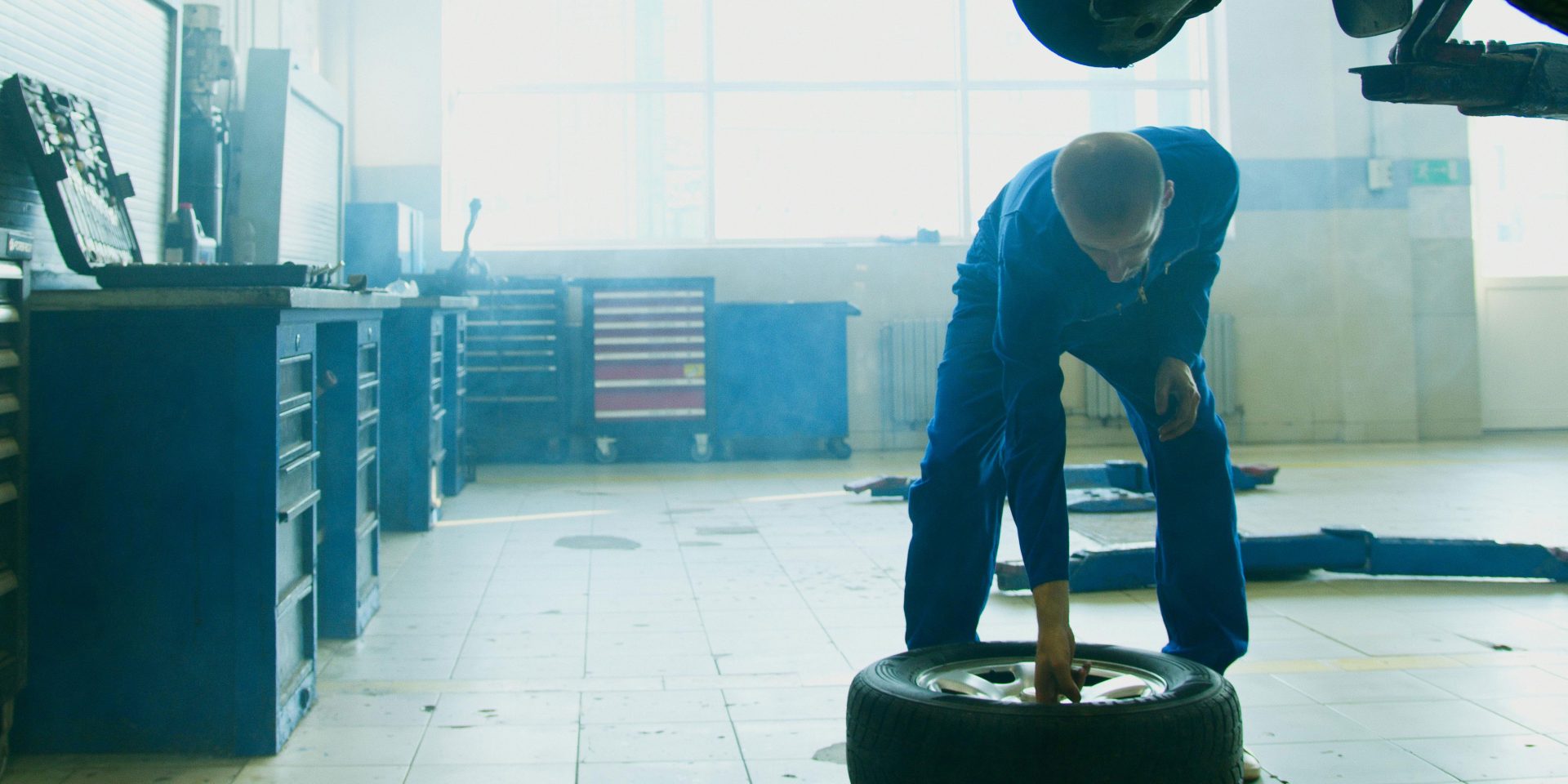 Mechanic in car shop picking up tire from the ground.