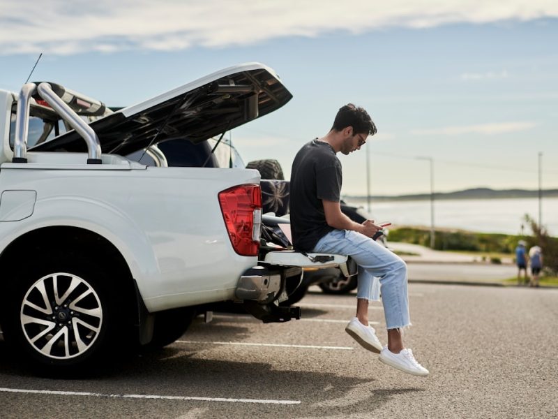 Man sitting on a car checking auto parts fitment on his smartphone in a driveway