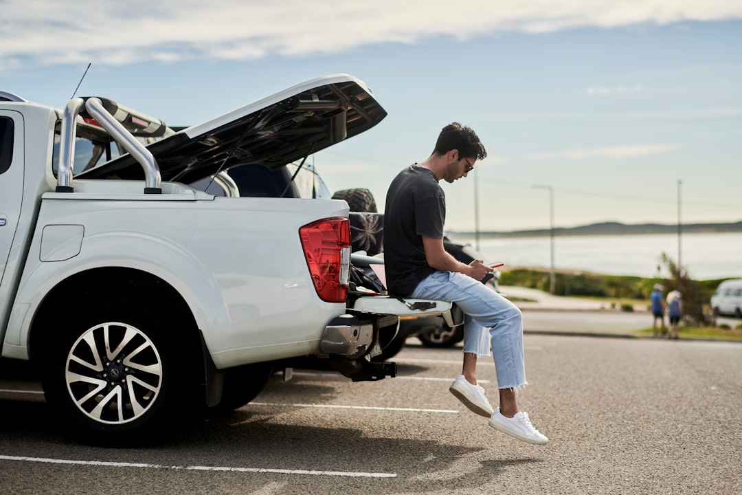 Man sitting on a car checking auto parts fitment on his smartphone in a driveway